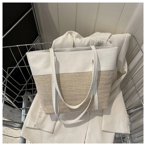 Detailed view of large straw tote bag with white leather stitching and herringbone weave