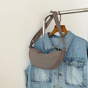Detail of taupe crescent crossbody bag with adjustable strap on denim background