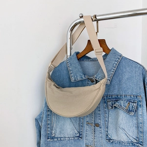 Detail of beige half-moon crossbody bag styled with a blue denim jacket on wood hanger