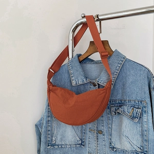 Detailed shot of a brick red crescent crossbody bag with adjustable wide strap on hanger