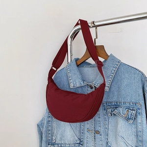 Detail of burgundy crescent moon nylon crossbody bag hanging on a metallic hanger