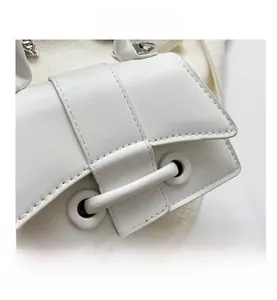 Detailed macro view of white handbag featuring textured flap and metallic chain ornament