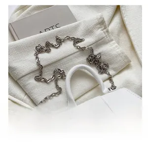 Detail of white leather handbag with silver chain strap on a beige tweed background