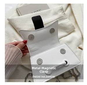 Close-up of white crossbody bag featuring silver magnetic buckles and metal chain strap