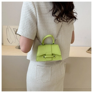 Model wearing a neon green mini crossbody bag with a silver chain and top handle
