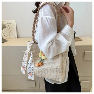 Detail of summer straw tote bag with elegant silk scarf and floral charm on shoulder