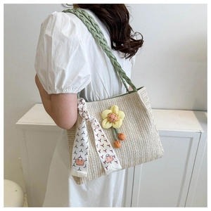 Detail of straw tote bag featuring green braided handle and yellow floral charm decoration