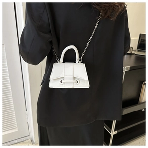 Close-up of white mini trapezoid handbag with silver chain strap on black blazer