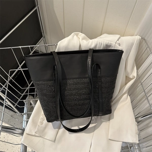 Large black patchwork straw tote bag with leather straps displayed in a modern setup