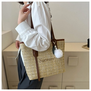 Detail of woven straw tote bag featuring brown leather trim and Summer embroidery detail