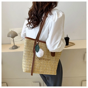 Detail of woven straw tote bag featuring leather straps and decorative pompom charm