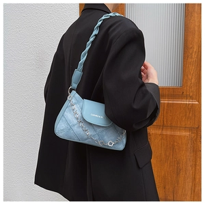 Detail of light blue denim shoulder bag featuring woven strap and heart chain charm