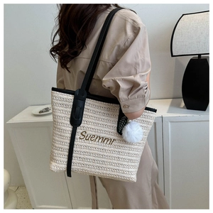 Detail of woven straw tote bag with Suemmr embroidery and plush ball charm on shoulder