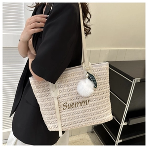 Close-up of beige woven tote bag with Suemmr embroidery and plush pom-pom charm detail