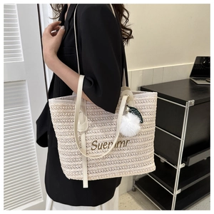 Detail of woven straw tote bag with Suernmr embroidery and plush ball charm accessory
