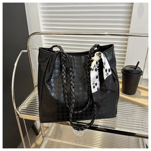 Detail of black houndstooth embossed tote bag featuring woven handles and silk scarf