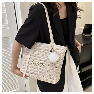 Close-up of woven straw tote bag featuring Suemmr embroidery and a pearl plush charm