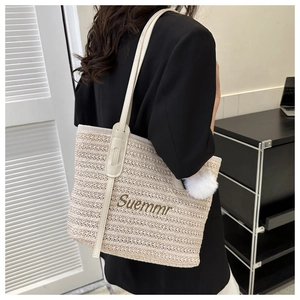 Detail of woven tote bag with Suemmr embroidery and white plush pompom charm on a shoulder strap