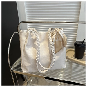 Detail view of a white woven tote bag with a decorative silk scarf on a glass shelf