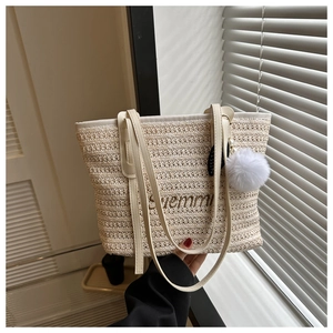 Detail of beige woven tote bag with brown embroidery and decorative pompom charm