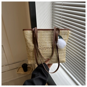 Detail of woven straw tote bag with Summer embroidery and brown leather shoulder strap