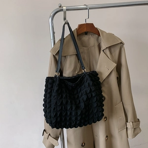 Detail of black bubble textured tote bag with leather straps and gold metal rings