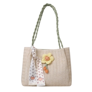 Large beige straw tote bag with green braided handles and a floral charm on white background