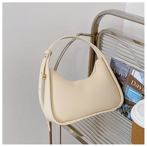Sac sous le bras croissant beige avec boucles dorées sur une chaise moderne