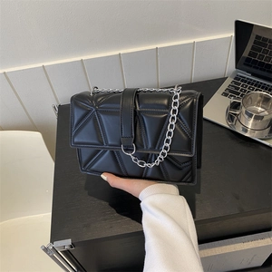 Borsa a tracolla nera trapuntata geometrica su una scrivania da ufficio moderna