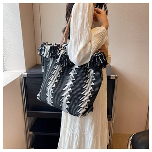 Close-up of black and white woven tote bag featuring fringe details and brown shoulder strap