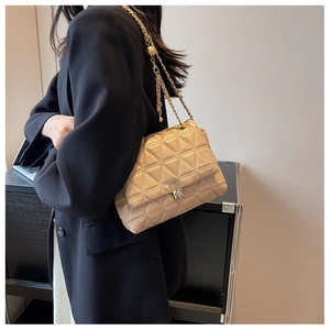 Detail of beige quilted shoulder bag with golden chain strap on model in indoor setting