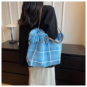 Close-up of blue woven tote bag with white grid patterns and long fringe details