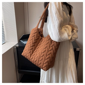 Detailed side view of a caramel quilted tote bag with leaf pattern texture on a model
