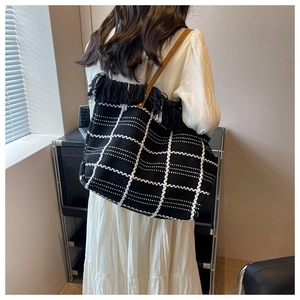 Detail of black woven tote bag with white checkered pattern and flowing fringe accents