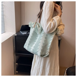 Detail of mint green woven tote with fringed edge and brown leather strap on model