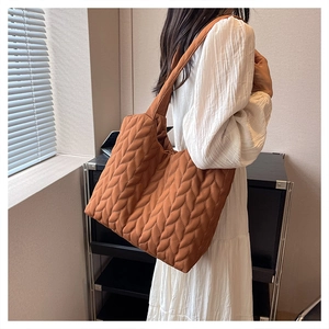 Detailed view of brown quilted tote bag with leaf pattern stitching worn on shoulder