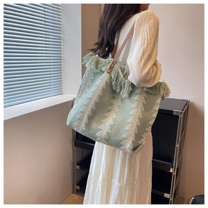 Detail of green woven tote bag showing fringe accents and leather shoulder straps