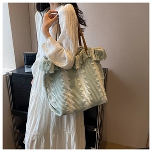 Detail view of woven tote bag with green chevron pattern and tassel fringe trim