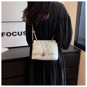 Close-up of white quilted crossbody bag with gold chain strap on black dress