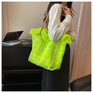 Detail of neon green woven tote bag with white checks, fringe edges and brown straps