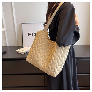 Detail of leaf-quilted shoulder tote bag in beige shown on a person for daily commute