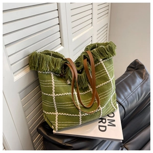 Close-up of green woven tote bag featuring white checkered patterns and thick fringe edges