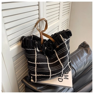 Detail of woven tote bag with black tassels and brown leather handles on a leather sofa