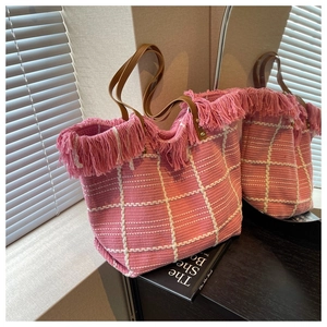 Detail of pink woven tote bag with fringe edges and brown leather handles on wooden surface