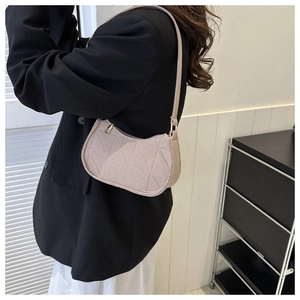 Close-up of beige quilted felt baguette bag worn on shoulder over a black blazer