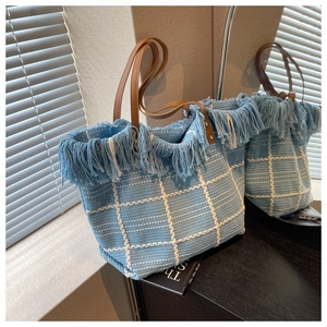Detail of blue and white woven tote bag with fringe trim and brown leather handles