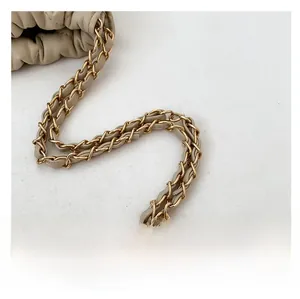 Detail of golden metal chain interwoven with beige leather strap on quilted handbag