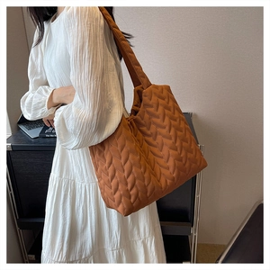 Quilted tote bag in brown nylon with wave-leaf stitching worn by a model in a dress