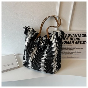 Macro detail of woven tote bag with geometric patterns, black and white fringes, and leather handles