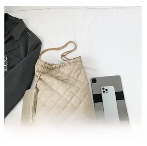 Detail of beige quilted tote bag with gold chain strap beside a tablet for size reference